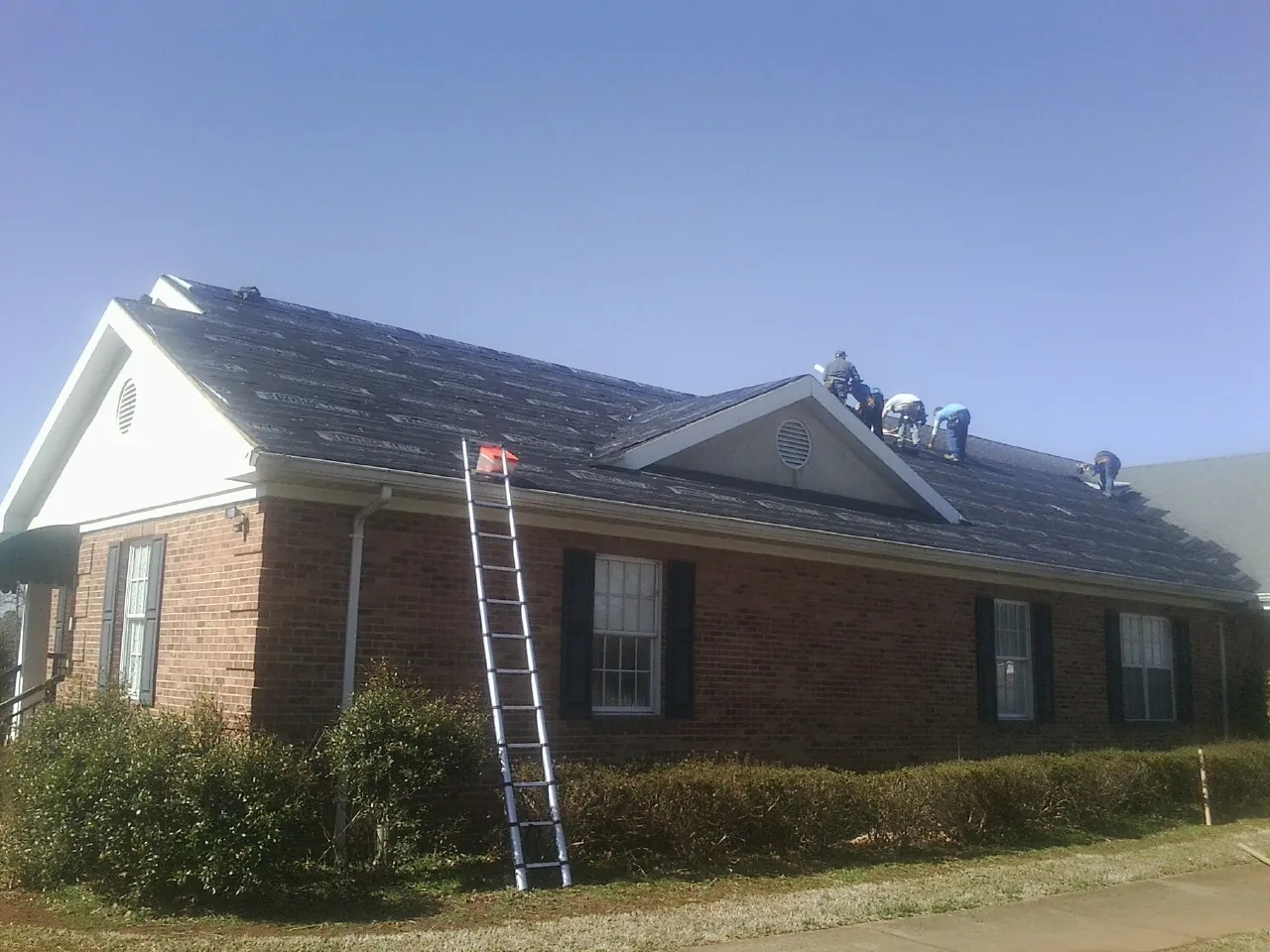Crew tearing shingles off a brick ranch roof with a ladder set — Emergency Roof Repair work by our crew in Coosawhatchie