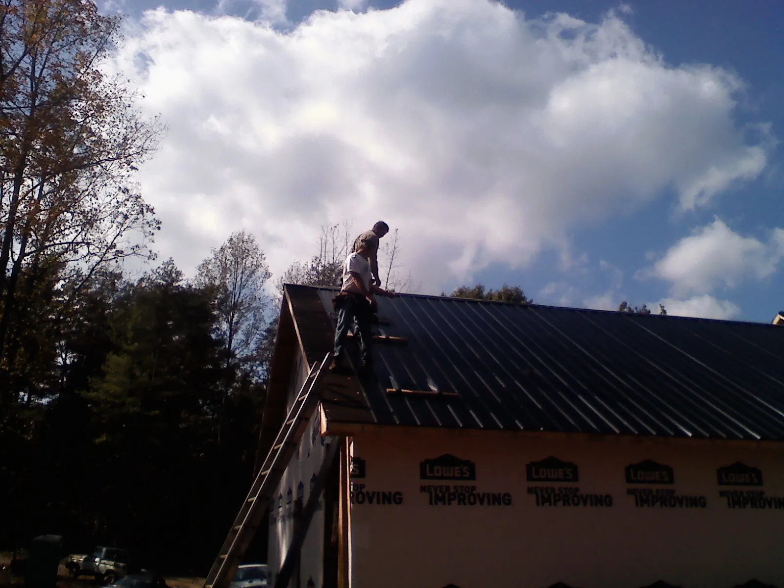 Roofer fastening dark metal panels high against a cloudy sky, from a Roof Inspection job in Coosawhatchie
