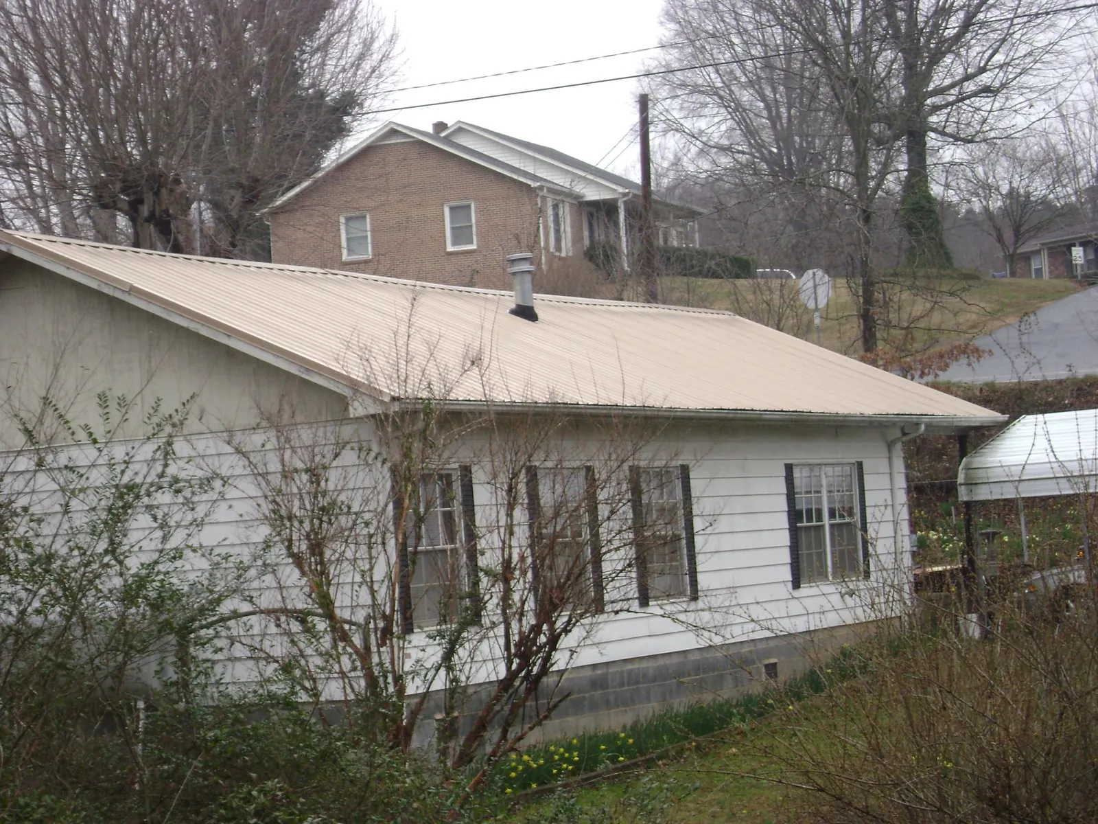 Tan metal roof on a white sided house set into a hillside — Commercial Roofing by Roofing Brothers in Coosawhatchie